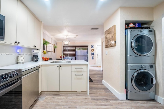 kitchen featuring appliances with stainless steel finishes, stacked washer and dryer, ornamental molding, kitchen peninsula, and light wood-type flooring