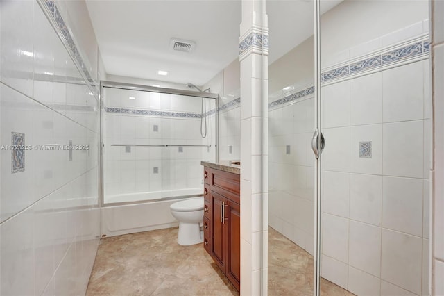 full bathroom with vanity, tile walls, bath / shower combo with glass door, and toilet