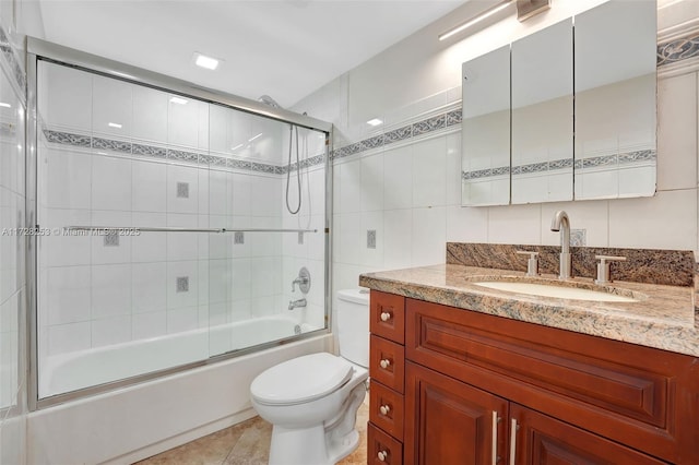 full bathroom featuring tile walls, shower / bath combination with glass door, tile patterned flooring, vanity, and toilet