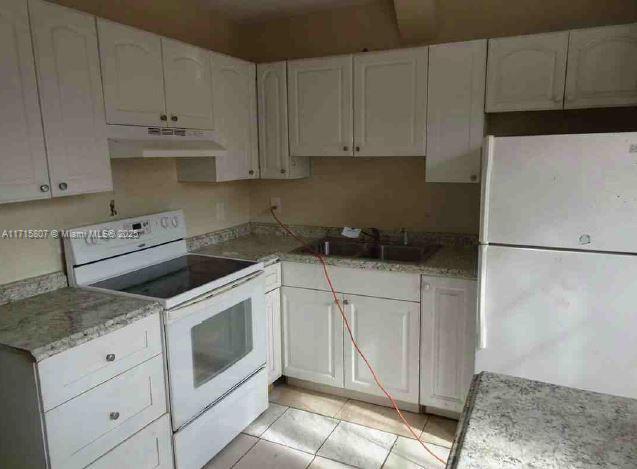 kitchen with light tile patterned floors, white appliances, sink, light stone counters, and white cabinets