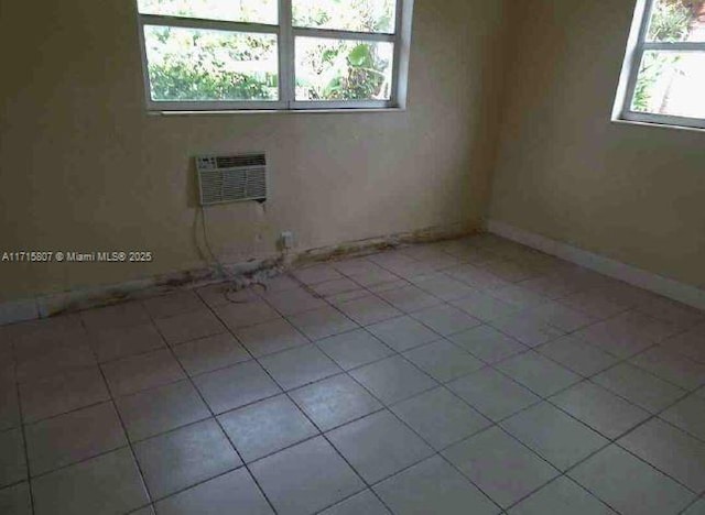 tiled spare room with a wall unit AC and a healthy amount of sunlight