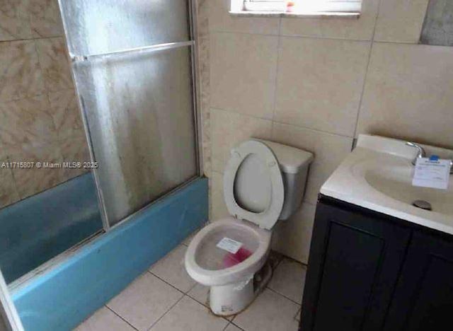 full bathroom featuring shower / bath combination with glass door, tile walls, vanity, tile patterned floors, and toilet