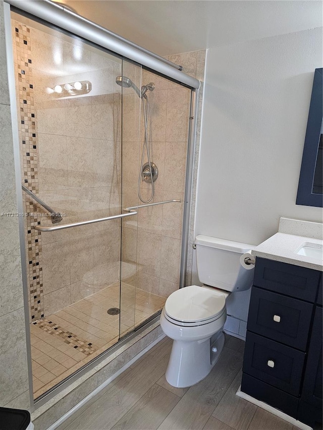 bathroom featuring vanity, hardwood / wood-style floors, a shower with shower door, and toilet