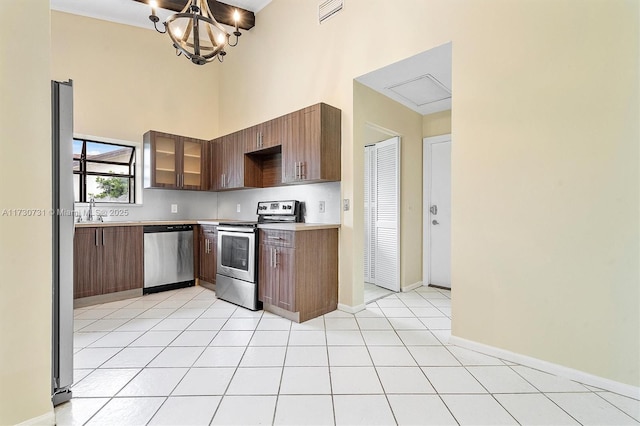 kitchen with a towering ceiling, sink, light tile patterned floors, a notable chandelier, and stainless steel appliances