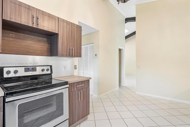 kitchen with light tile patterned floors, a towering ceiling, and stainless steel range with electric cooktop