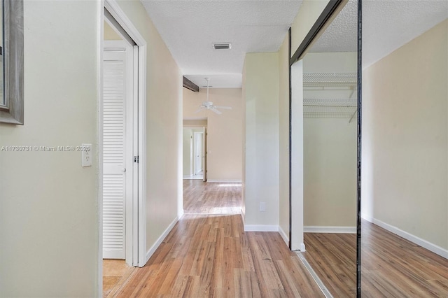 hallway with a textured ceiling and light wood-type flooring