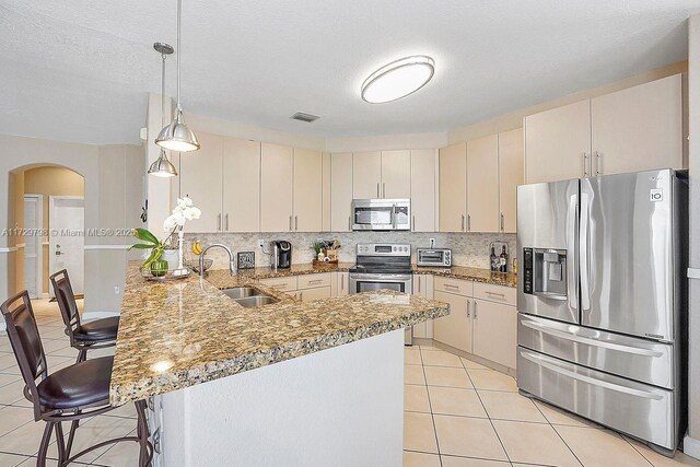 kitchen featuring sink, a breakfast bar, appliances with stainless steel finishes, decorative light fixtures, and kitchen peninsula