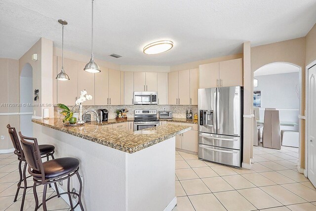 kitchen with stone counters, light tile patterned flooring, backsplash, kitchen peninsula, and stainless steel appliances