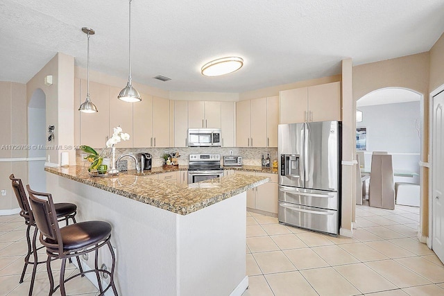 kitchen featuring appliances with stainless steel finishes, light tile patterned flooring, a peninsula, and tasteful backsplash