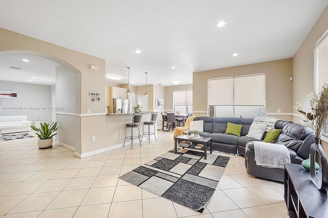 living room featuring arched walkways, light tile patterned flooring, baseboards, and recessed lighting