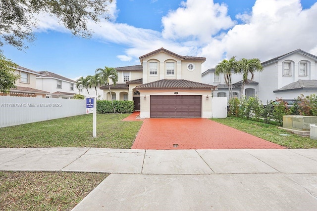 mediterranean / spanish home with a tile roof, fence, decorative driveway, a front lawn, and stucco siding