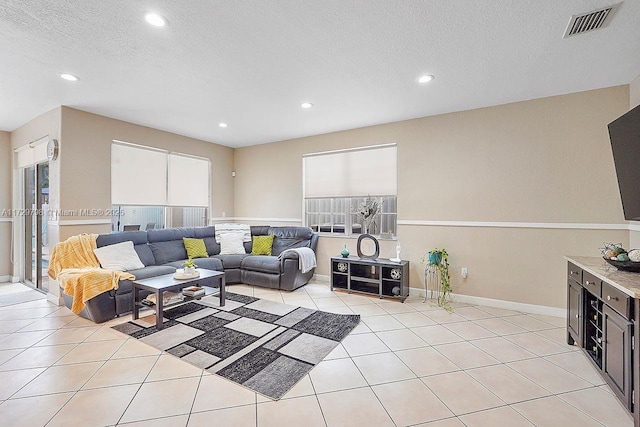 living room featuring light tile patterned floors, baseboards, visible vents, a textured ceiling, and recessed lighting