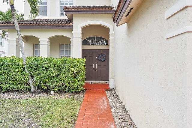 view of exterior entry with a tile roof and stucco siding