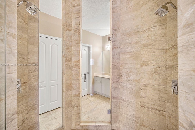 full bathroom with a textured ceiling, tiled shower, and vanity