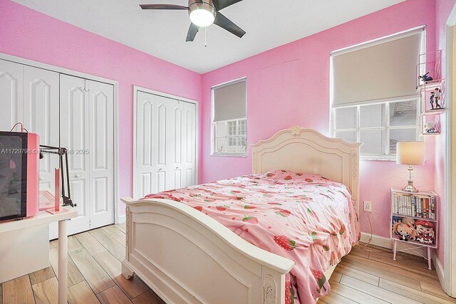 bedroom featuring ceiling fan, light hardwood / wood-style flooring, and two closets