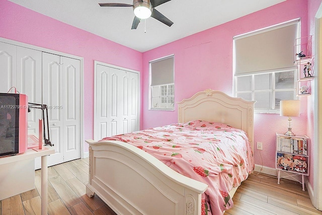 bedroom featuring light wood finished floors, a ceiling fan, baseboards, and multiple closets