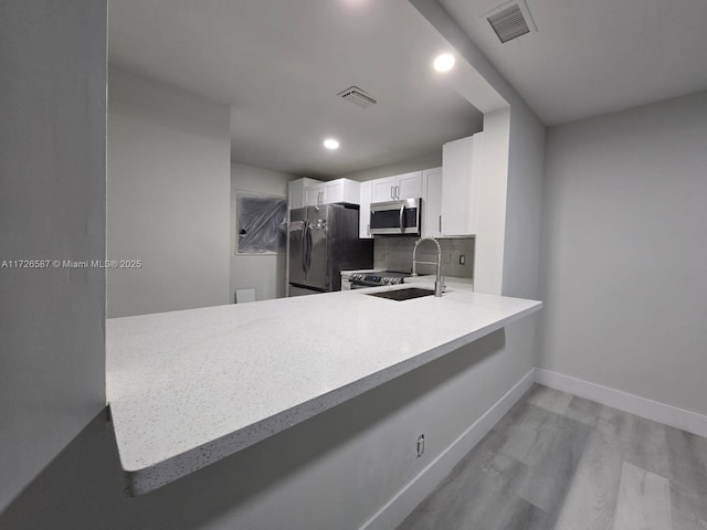 kitchen featuring light hardwood / wood-style flooring, backsplash, stainless steel appliances, white cabinets, and kitchen peninsula