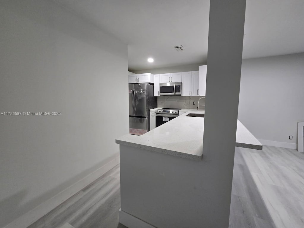 kitchen with appliances with stainless steel finishes, tasteful backsplash, white cabinetry, kitchen peninsula, and light hardwood / wood-style flooring