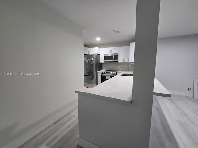 kitchen with appliances with stainless steel finishes, tasteful backsplash, white cabinetry, kitchen peninsula, and light hardwood / wood-style flooring