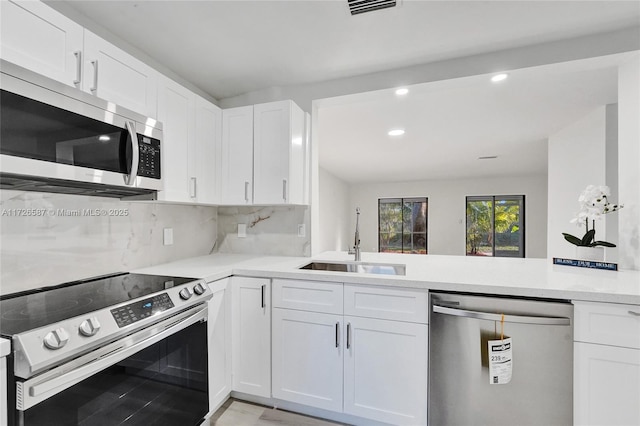 kitchen featuring sink, stainless steel appliances, kitchen peninsula, white cabinets, and decorative backsplash