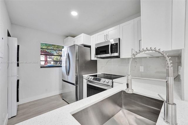 kitchen with light hardwood / wood-style floors, stainless steel appliances, white cabinetry, and light stone countertops