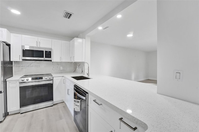 kitchen with appliances with stainless steel finishes, sink, backsplash, light wood-type flooring, and white cabinets