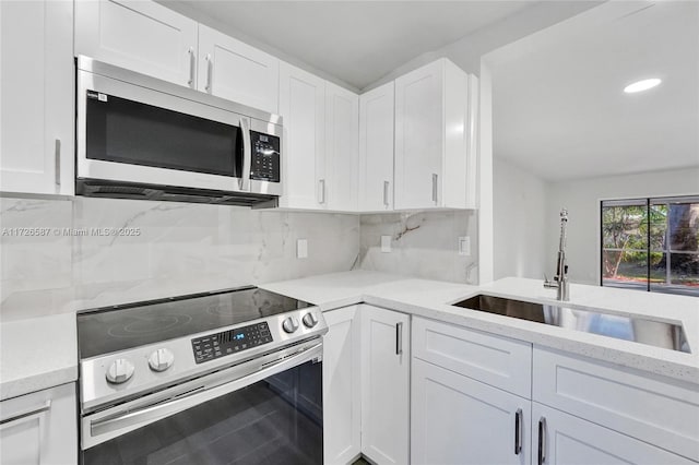 kitchen featuring stainless steel appliances, sink, backsplash, light stone counters, and white cabinets