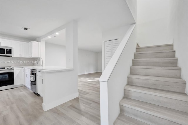 kitchen featuring light wood-type flooring, stainless steel electric range oven, white cabinets, and decorative backsplash