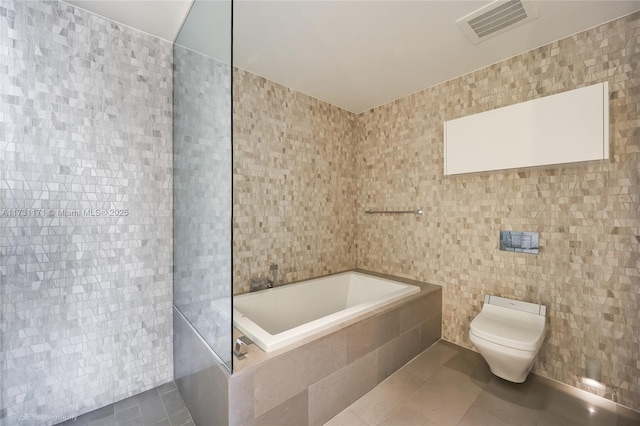 bathroom featuring a relaxing tiled tub, toilet, tile patterned flooring, and tile walls