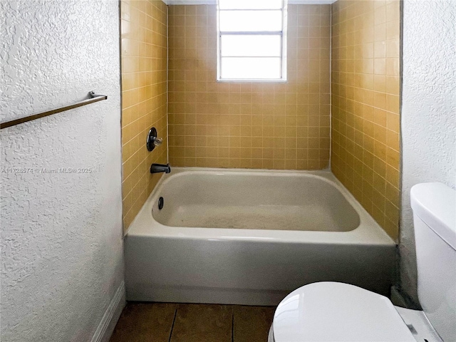 bathroom featuring tile patterned flooring, tiled shower / bath combo, and toilet