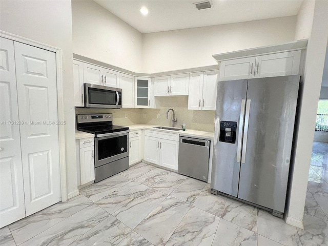 kitchen with appliances with stainless steel finishes, sink, white cabinets, and a towering ceiling