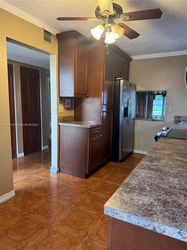 kitchen with stainless steel refrigerator with ice dispenser, stove, ceiling fan, and a textured ceiling