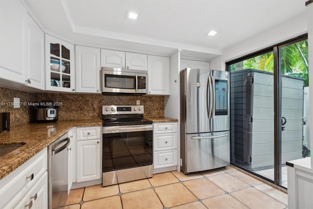 kitchen with tasteful backsplash, stainless steel appliances, dark stone counters, and white cabinets