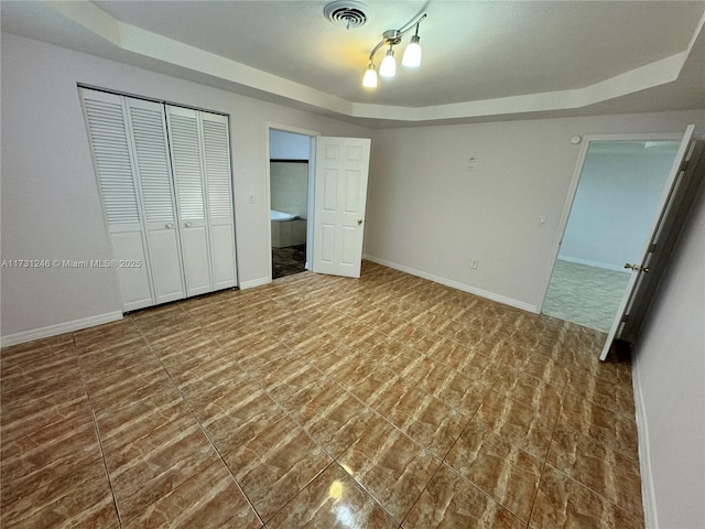 unfurnished bedroom with ensuite bath, a tray ceiling, and a closet