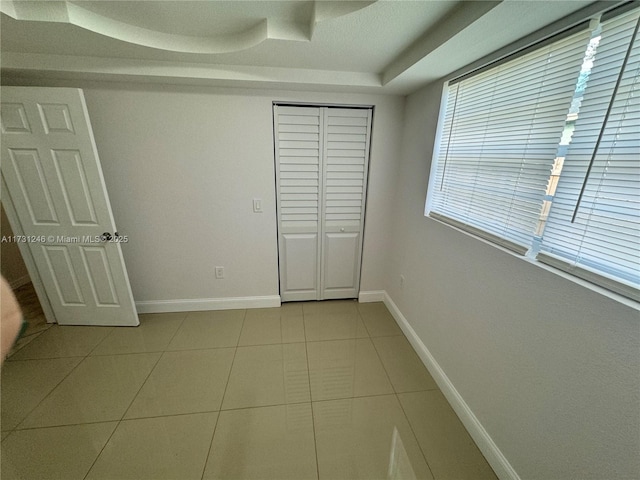 unfurnished bedroom featuring light tile patterned flooring and a tray ceiling