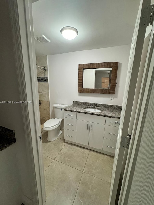 bathroom with tile patterned flooring, vanity, tiled shower, and toilet