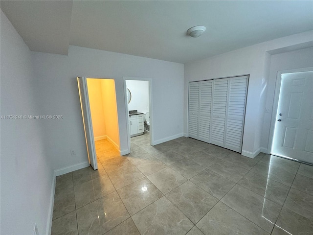 unfurnished bedroom with connected bathroom, a closet, and light tile patterned floors