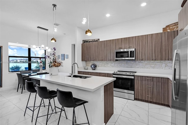 kitchen featuring sink, hanging light fixtures, an island with sink, stainless steel appliances, and decorative backsplash