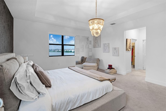 carpeted bedroom with a walk in closet, a chandelier, and a tray ceiling