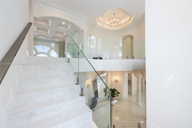 staircase featuring a high ceiling, ornamental molding, coffered ceiling, and a chandelier