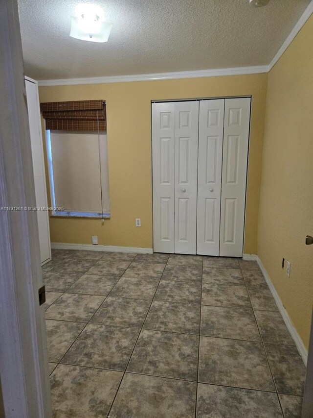 unfurnished bedroom featuring dark tile patterned floors, crown molding, a textured ceiling, and a closet