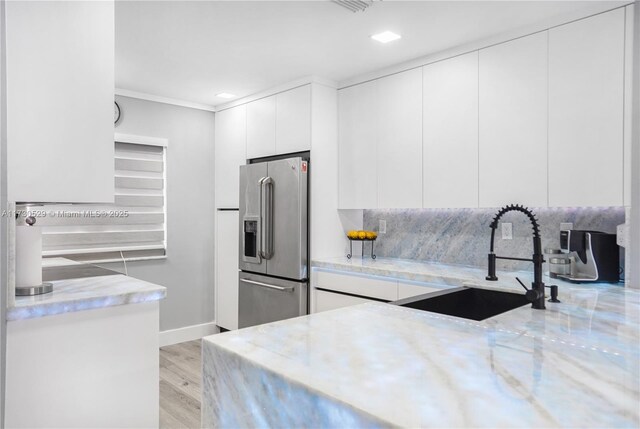 kitchen with high quality fridge, white cabinets, light wood-type flooring, and kitchen peninsula