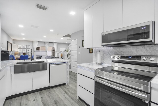 kitchen featuring sink, high end fridge, white cabinetry, light stone countertops, and light wood-type flooring