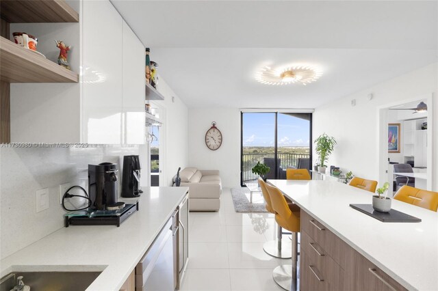 kitchen featuring expansive windows, stainless steel dishwasher, light tile patterned floors, and white cabinets