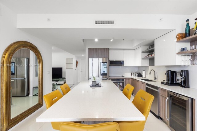 kitchen with sink, a kitchen breakfast bar, stainless steel appliances, white cabinets, and beverage cooler