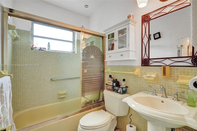 full bathroom with bath / shower combo with glass door, sink, tile walls, decorative backsplash, and toilet