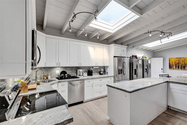 kitchen featuring sink, appliances with stainless steel finishes, white cabinetry, lofted ceiling with skylight, and light stone counters