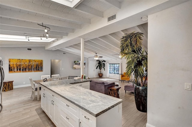 kitchen with vaulted ceiling with beams, wood ceiling, light stone countertops, light hardwood / wood-style floors, and white cabinets