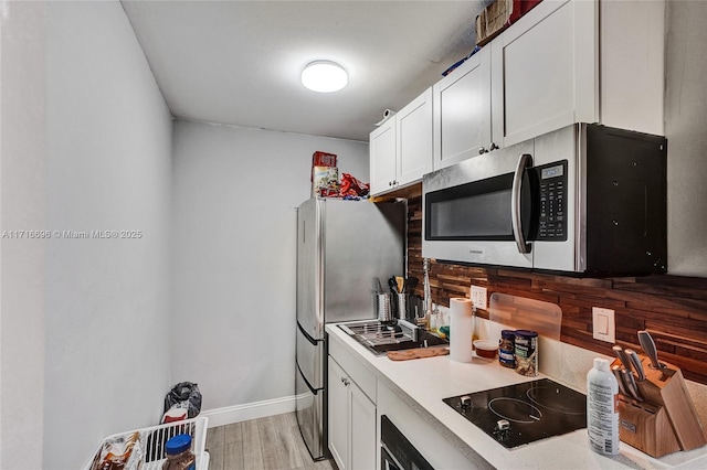 kitchen with backsplash, appliances with stainless steel finishes, light hardwood / wood-style floors, and white cabinets