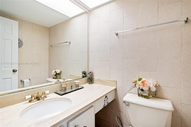 bathroom featuring tile walls, vanity, a skylight, and toilet
